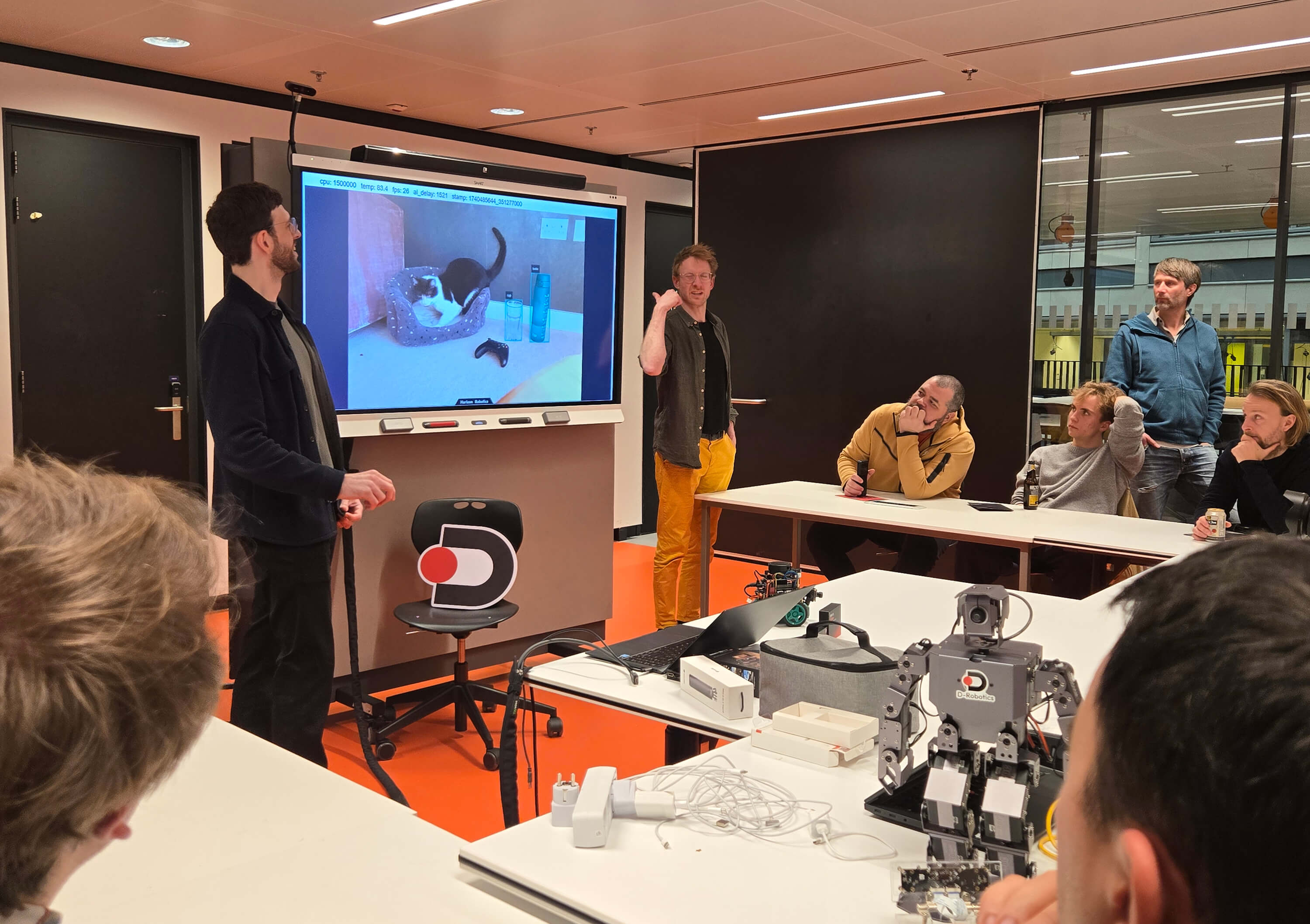 In the D-Robotics meet-up, some people explain around the projection screen. There are humanoid robots and other devices on the table. Everyone focuses on interaction, showing the atmosphere of technical communication.
